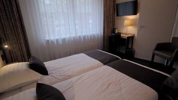 Quarto de hotel com duas camas, uma escrivaninha com lâmpada, televisão e uma cadeira.