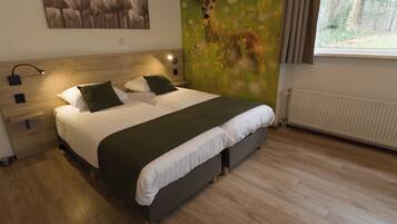 Un dormitorio moderno con cabecera de madera, una cama grande con ropa blanca y almohadas verdes, una mesita de noche con lámpara, y un mural en la pared con un ciervo en un campo.
