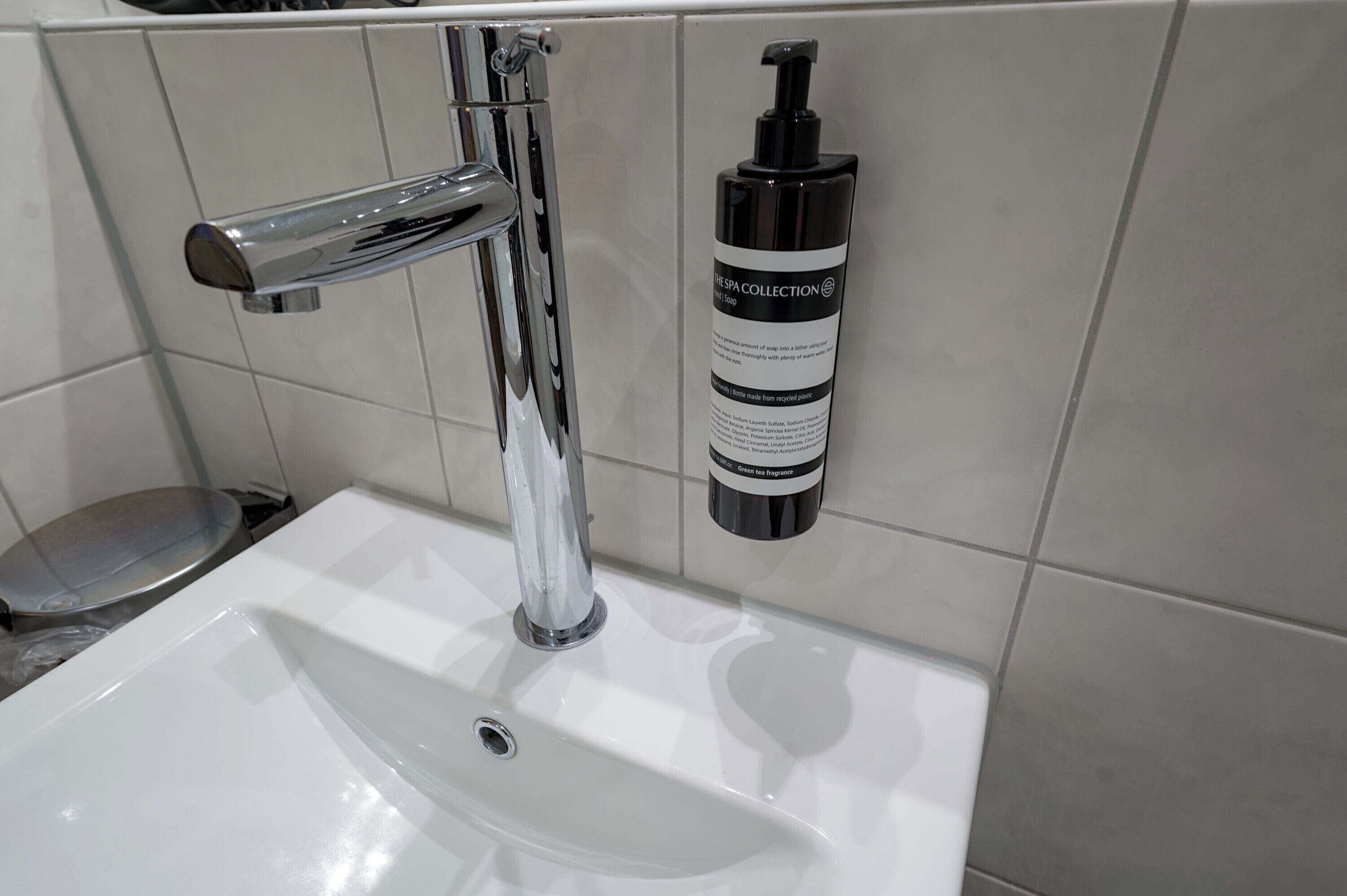 A bathroom sink with a chrome faucet and a bottle of green fragrance soap.