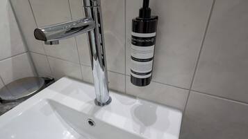 A bathroom sink with a chrome faucet and a bottle of green fragrance soap.