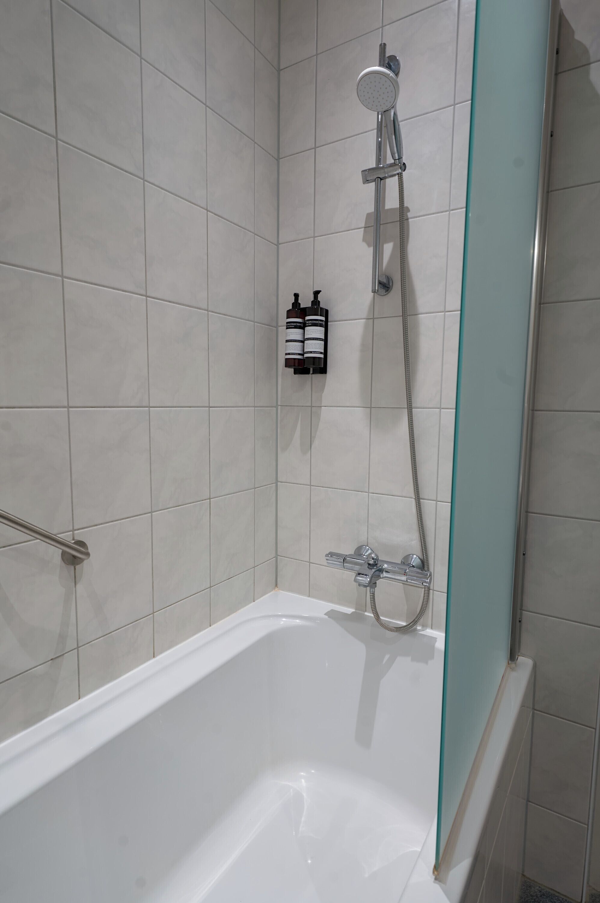 A modern bathroom with a white bathtub, a glass shower enclosure, and a handheld showerhead.
