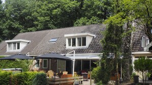 Une maison à deux étages, dotée d’un toit en pente, d’un porche couvert et d’un patio aménagé avec du mobilier d’extérieur.