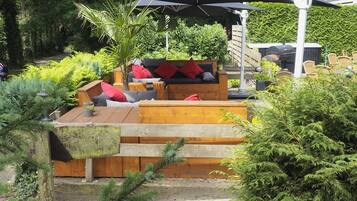 A patio area with a wooden bench, a black umbrella, and a grill.