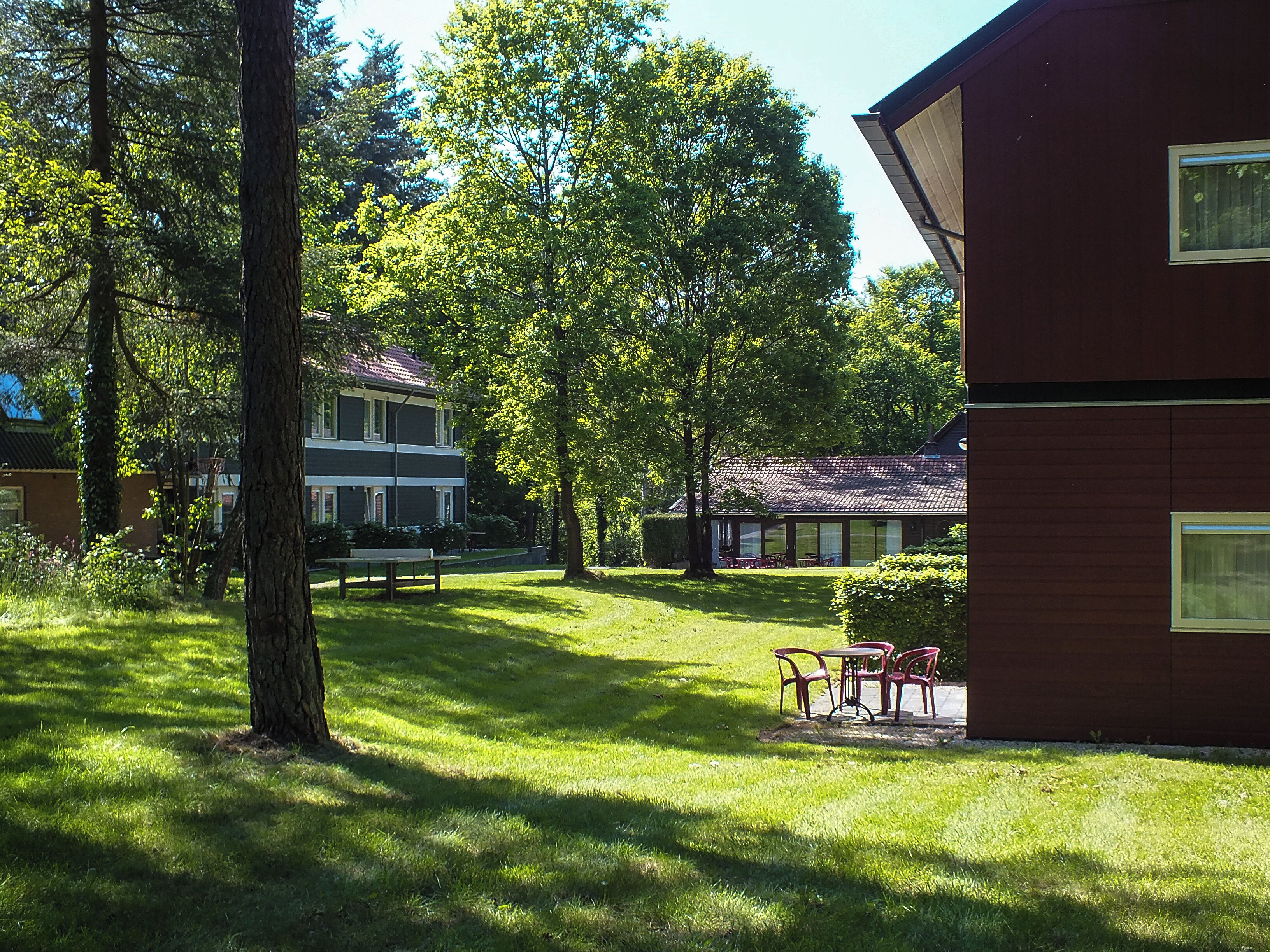 A two-story building with a red exterior, surrounded by lush green trees and grass.