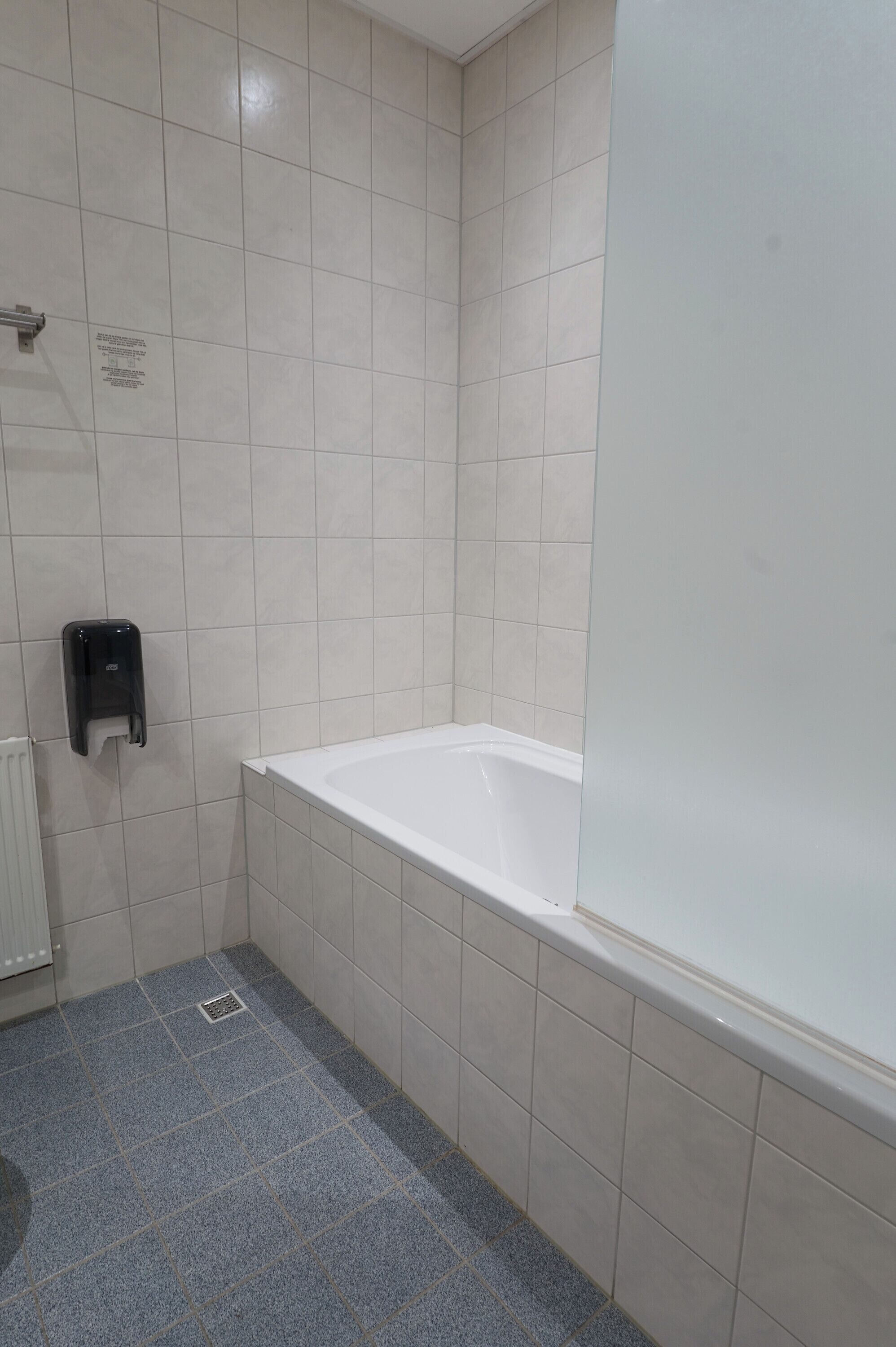 A bathroom with a bathtub, a hand dryer, and a vent.