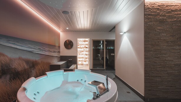 Un spa moderno con una bañera de hidromasaje grande, techo de madera y vista al océano a través de un ventanal.