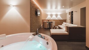 Un moderno cuarto de spa con hidromasaje, una zona de estar con una mesa y sillas, y un televisor montado en la pared.