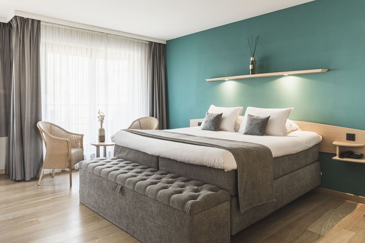 A modern bedroom with a large bed, a bench, a chair, and a small table.