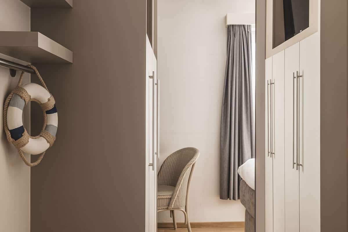 A modern, minimalist room with a wooden floor, a wicker chair, a wardrobe, and a curtain.
