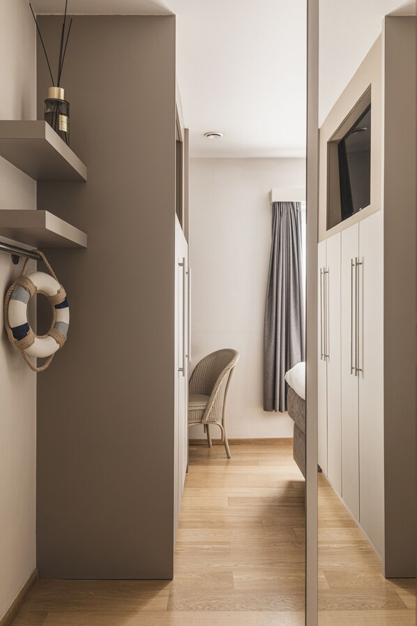 A modern, minimalist room with a wooden floor, a wicker chair, a wardrobe, and a curtain. - Boutique Hotel Hof ter Duinen (Koksijde)