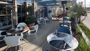 Un café al aire libre con mesas, sillas, sombrillas y un edificio al fondo.