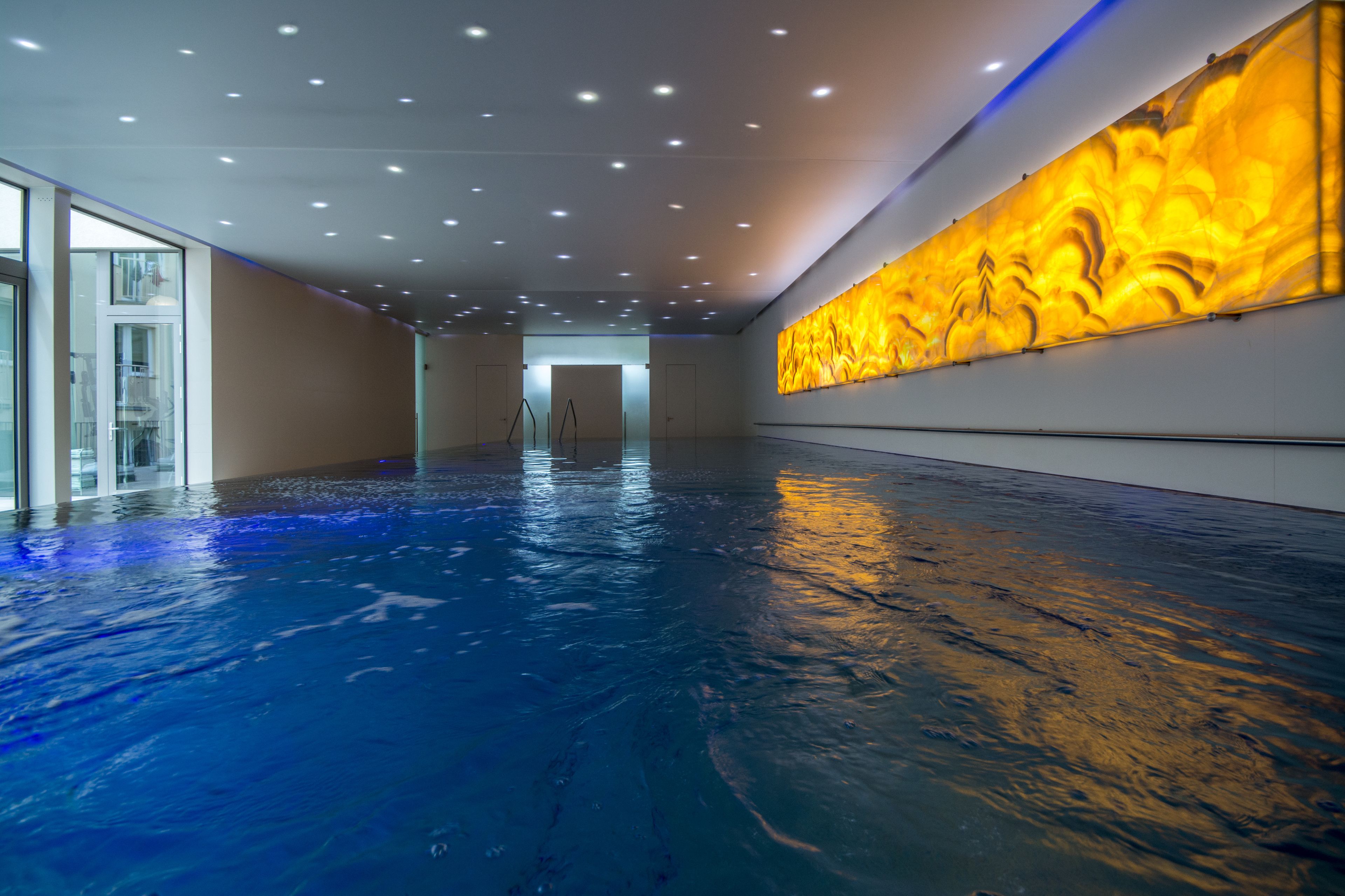 Una amplia piscina cubierta con suelo reflectante, un mural grande en la pared y un ascensor de vidrio.