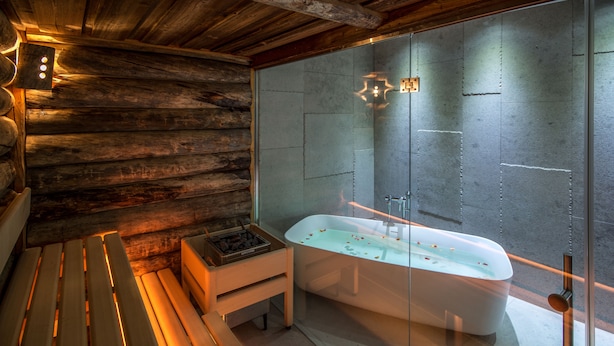 Een moderne badkamer met een vrijstaand bad, houten bankjes en een stenen muur.