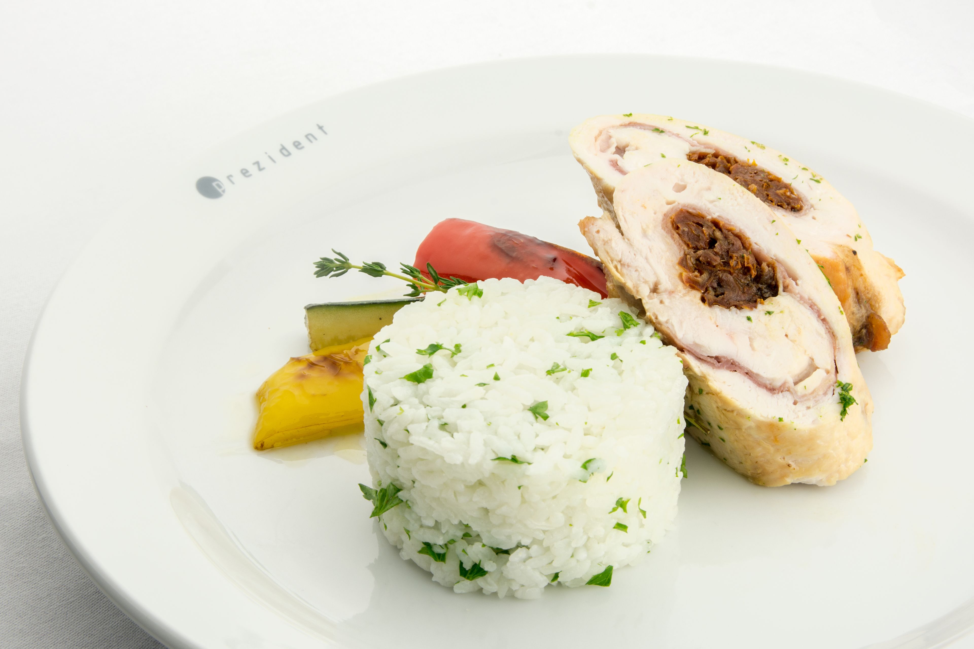 A plate with white rice, a slice of meat with stuffing, a red tomato, and a yellow vegetable.