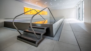 Een moderne trap met metalen leuningen, een glazen balustrade en een wanddecoratie met structuur.