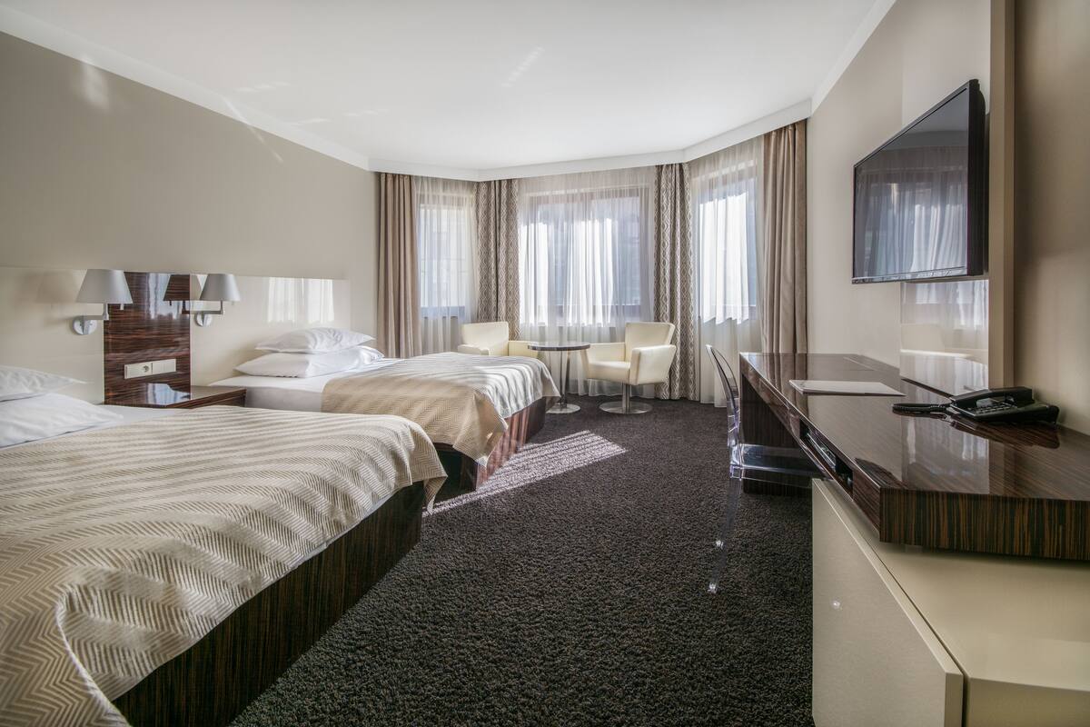 Une chambre d’hôtel avec deux lits, un bureau, une chaise, une télévision et une fenêtre avec des rideaux.