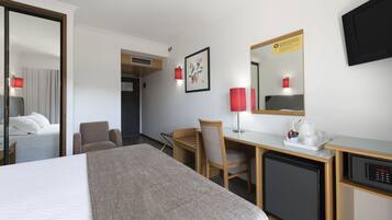 Una habitación de hotel con cama, escritorio, silla y un refrigerador pequeño.
