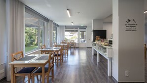 Un espace de restauration moderne avec des tables et des chaises en bois, de grandes fenêtres et une vue sur la verdure environnante.