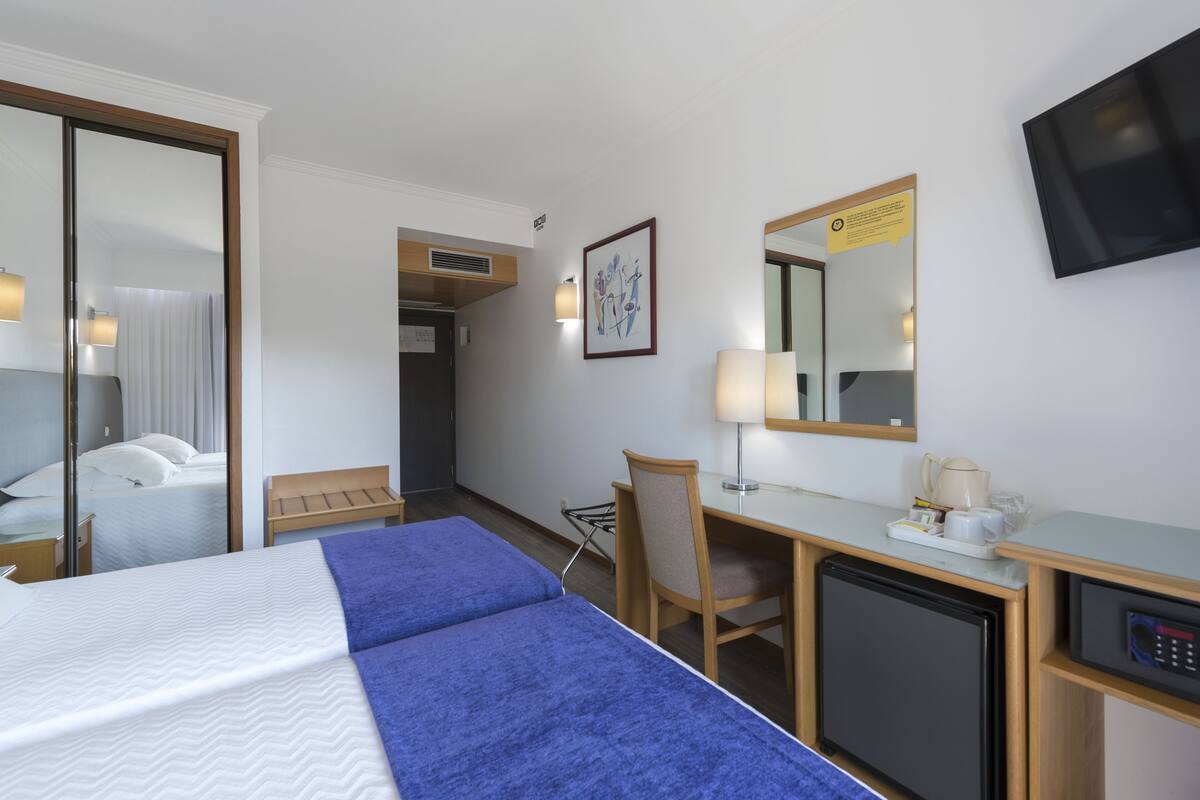 Ein Hotelzimmer mit Bett, Schreibtisch, Sessel, Fernseher und Spiegel.
