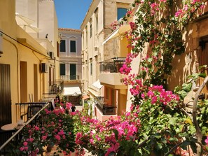 A narrow street with buildings on either side, balconies with railings, and a small outdoor seating area with tables and chairs. - Iason Studios (Chania)