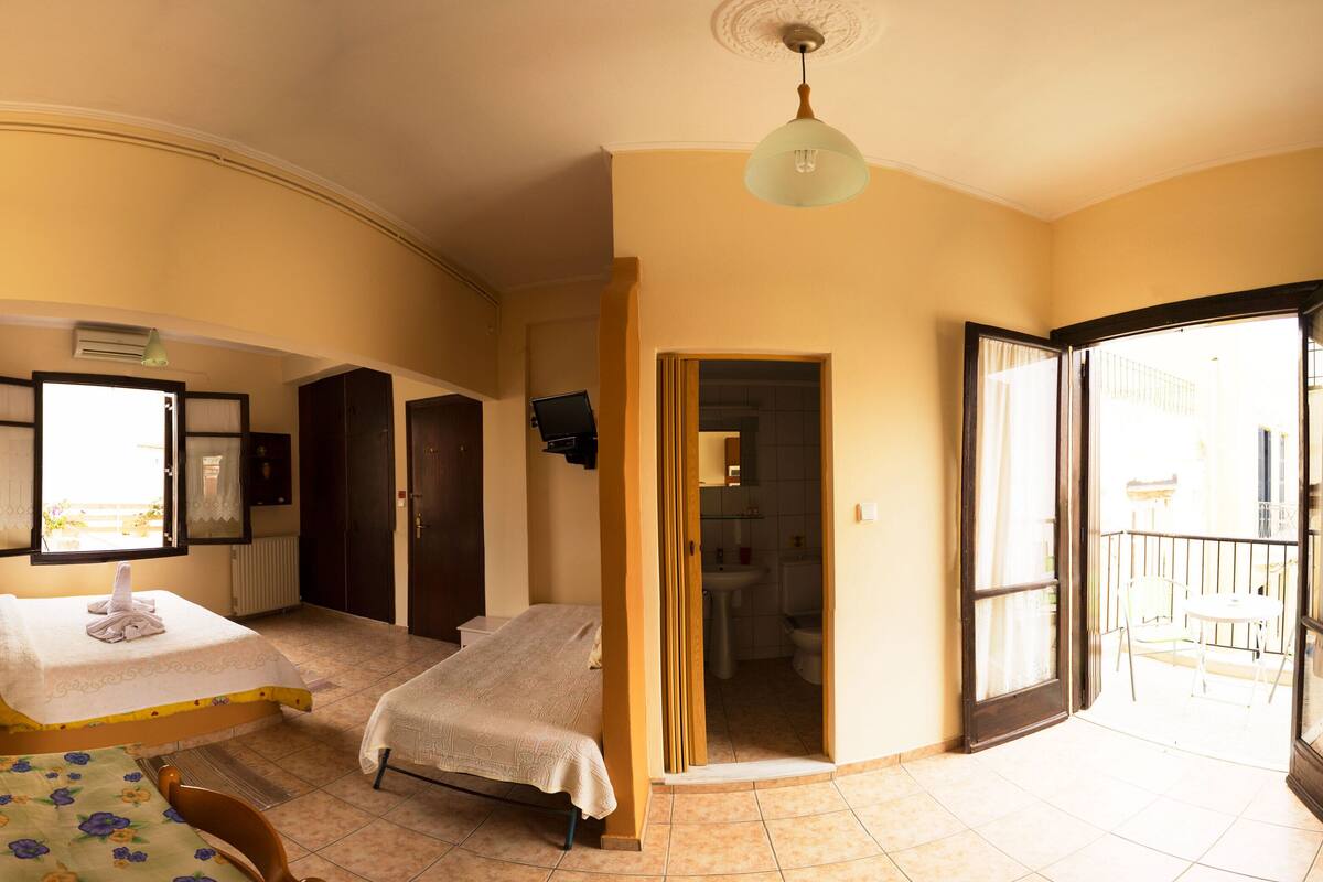 A hotel room with two beds, a sitting area with a table and chairs, a bathroom, and a balcony.