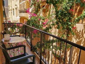 A balcony with a table and chairs, a railing, and a building with pink flowers. - Iason Studios (Chania)