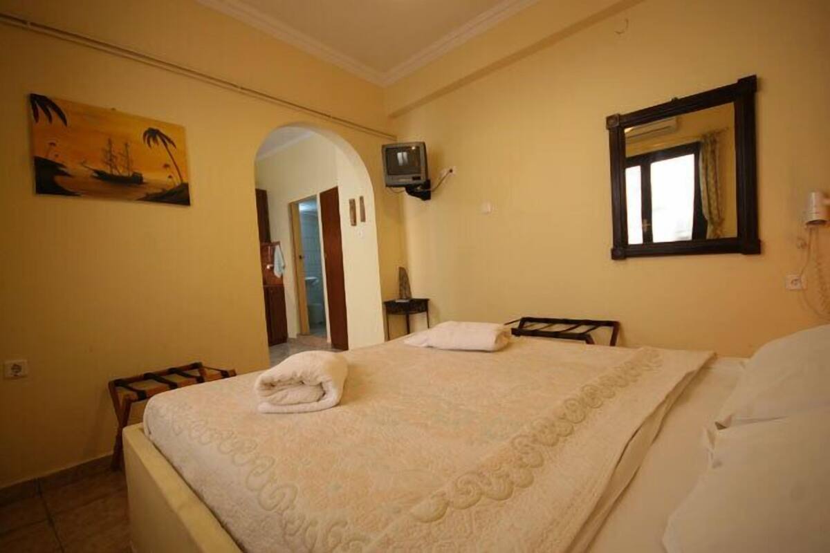 A hotel room with a bed, a television, a painting, and a mirror.
