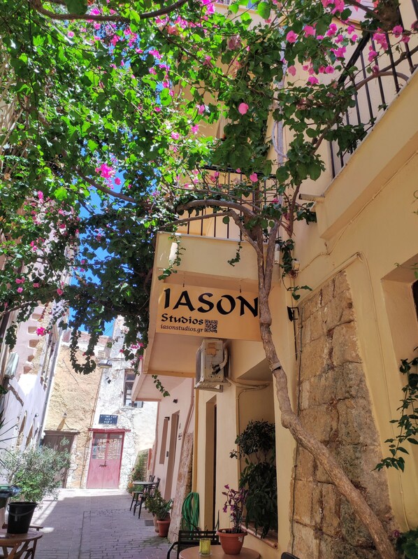 A narrow street with a building labeled "IASON Studios" and a tree with pink flowers. - Iason Studios (Chania)