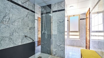 Une salle de bain moderne avec des murs en marbre, une douche à parois de verre et un banc jaune.