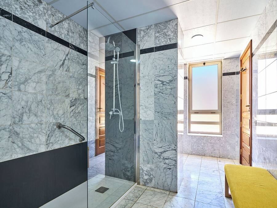 Une salle de bain moderne avec des murs en marbre, une douche à parois de verre et un banc jaune.