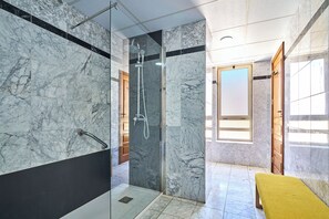 Un baño moderno con paredes de mármol, ducha con cerramiento de vidrio y un banco amarillo.