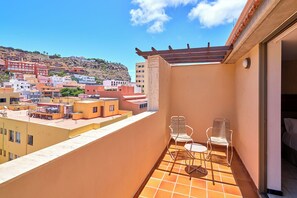 Un balcón con vistas a un pueblo en la ladera, una pérgola y dos sillas.