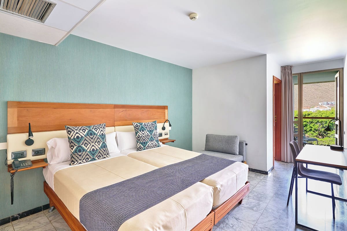 Una habitación de hotel con cama, mesita de noche, lámpara y vistas al exterior.