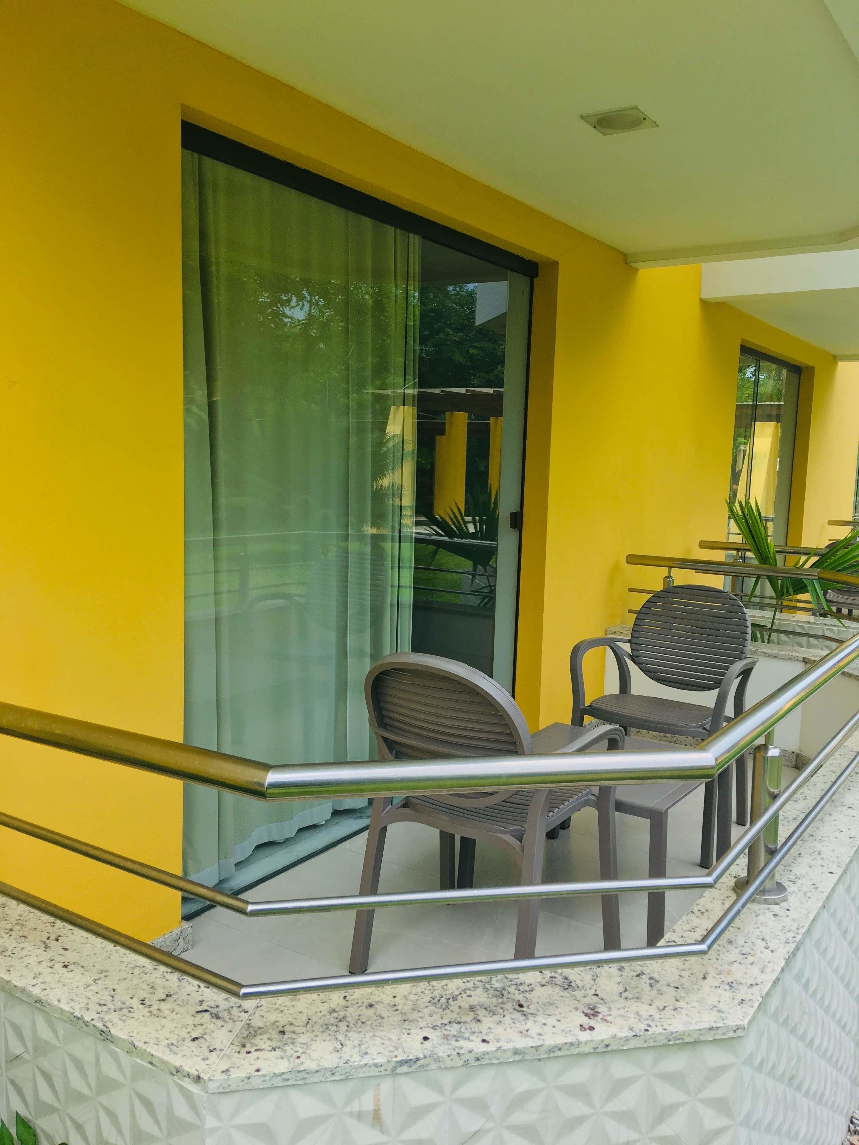 Ein Balkon mit zwei Stühlen, einem Tisch und einer Glastür, an einer gelben Wand.