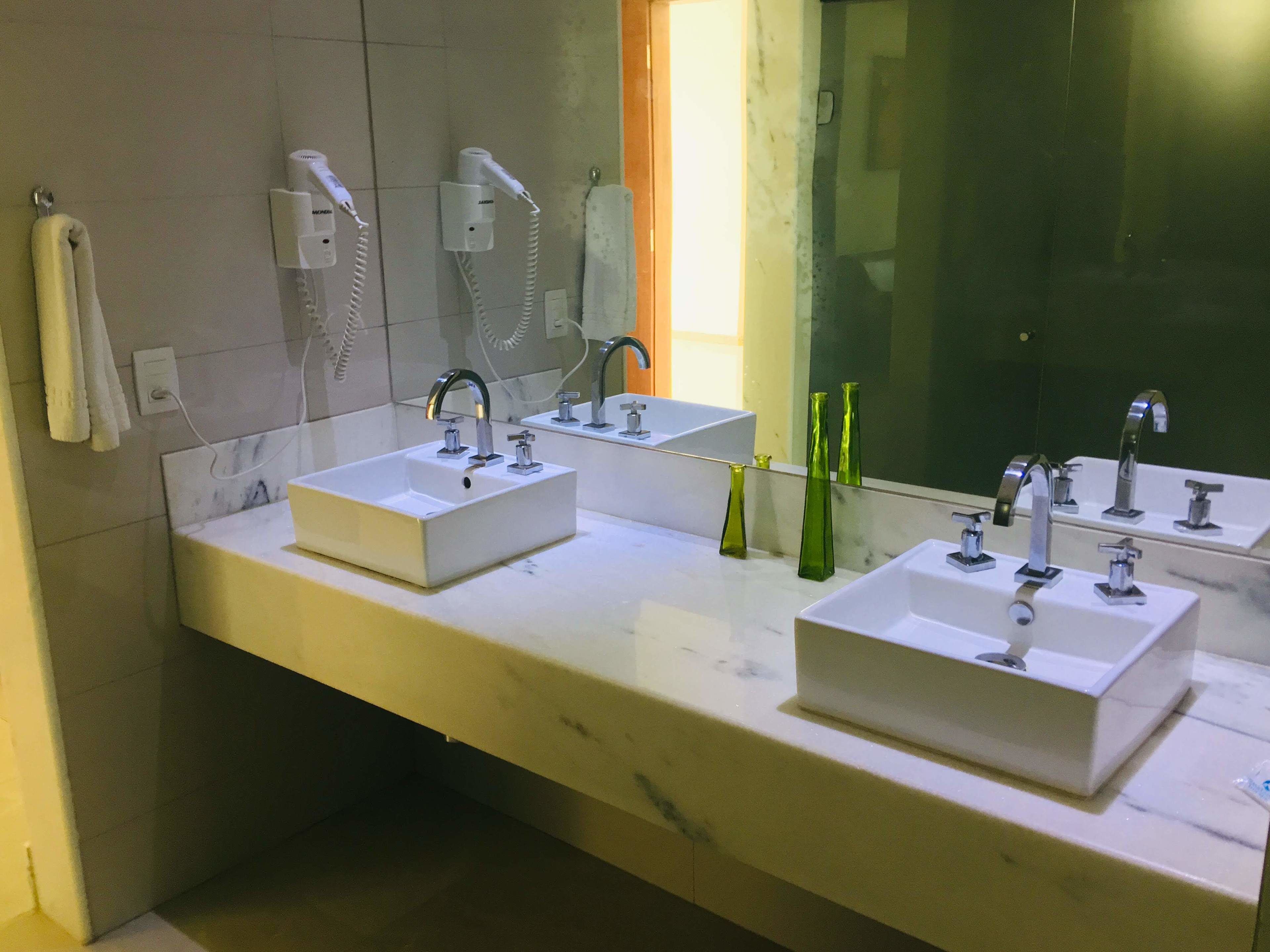 A bathroom with two sinks, a mirror, and a hairdryer on the wall.