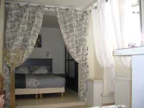 A bedroom with a bed, a bedside table, a radiator, and a window with curtains. - Hôtel de l'Europe (Paris)