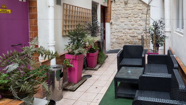 A small courtyard with wicker furniture, potted plants, and a stone wall. - Hôtel de l'Europe (Paris)