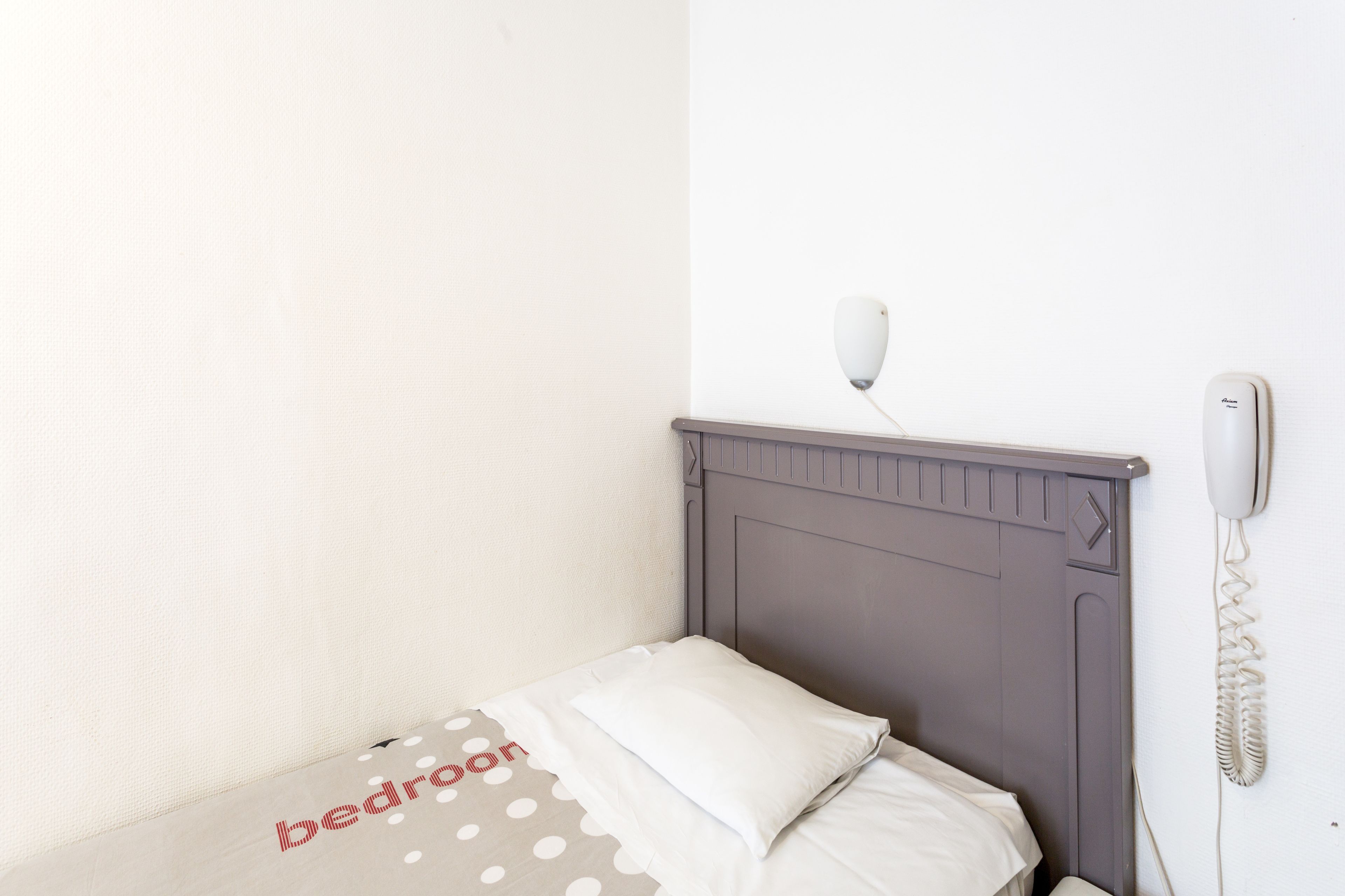 A single bed with a headboard, a bedside telephone, and a wall-mounted light fixture.