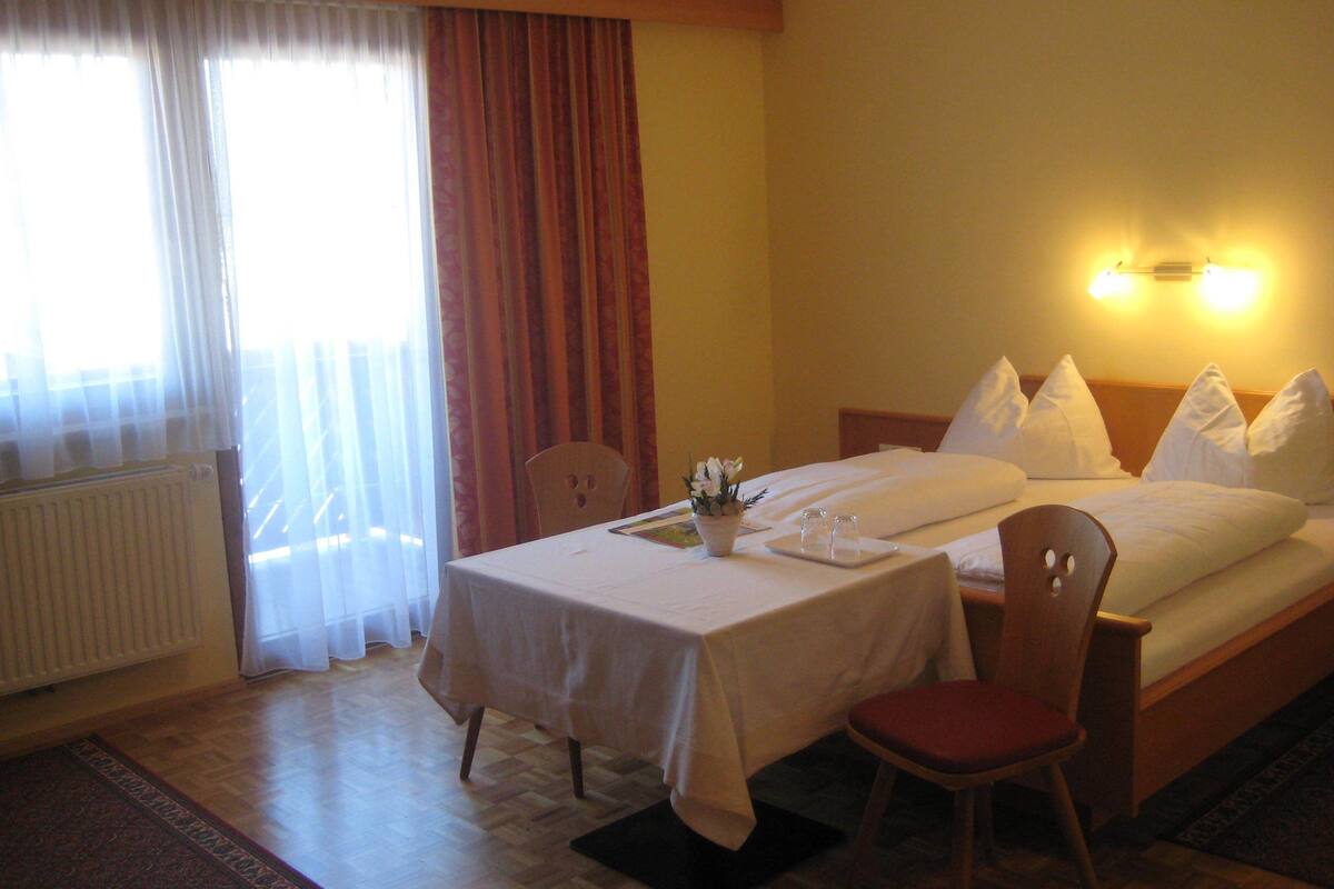 Una habitación de hotel con cama, una mesa con mantel blanco, una silla y una mesita con un florero.