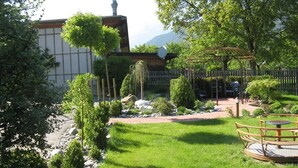 Ein gepflegter Garten mit einer Pergola, einer Sitzgelegenheit und Blick auf einen Berg im Hintergrund.