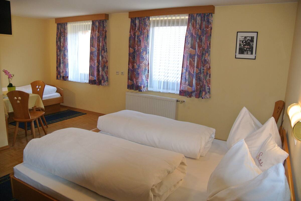 Habitación de hotel con dos camas individuales, una silla de madera, una mesita y un radiador.
