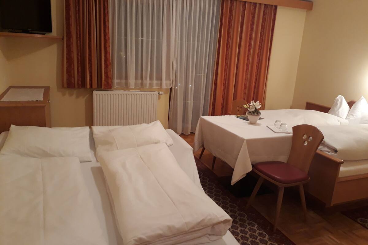Habitación de hotel con dos camas, una mesa con un florero, una silla y un televisor sobre una estantería.