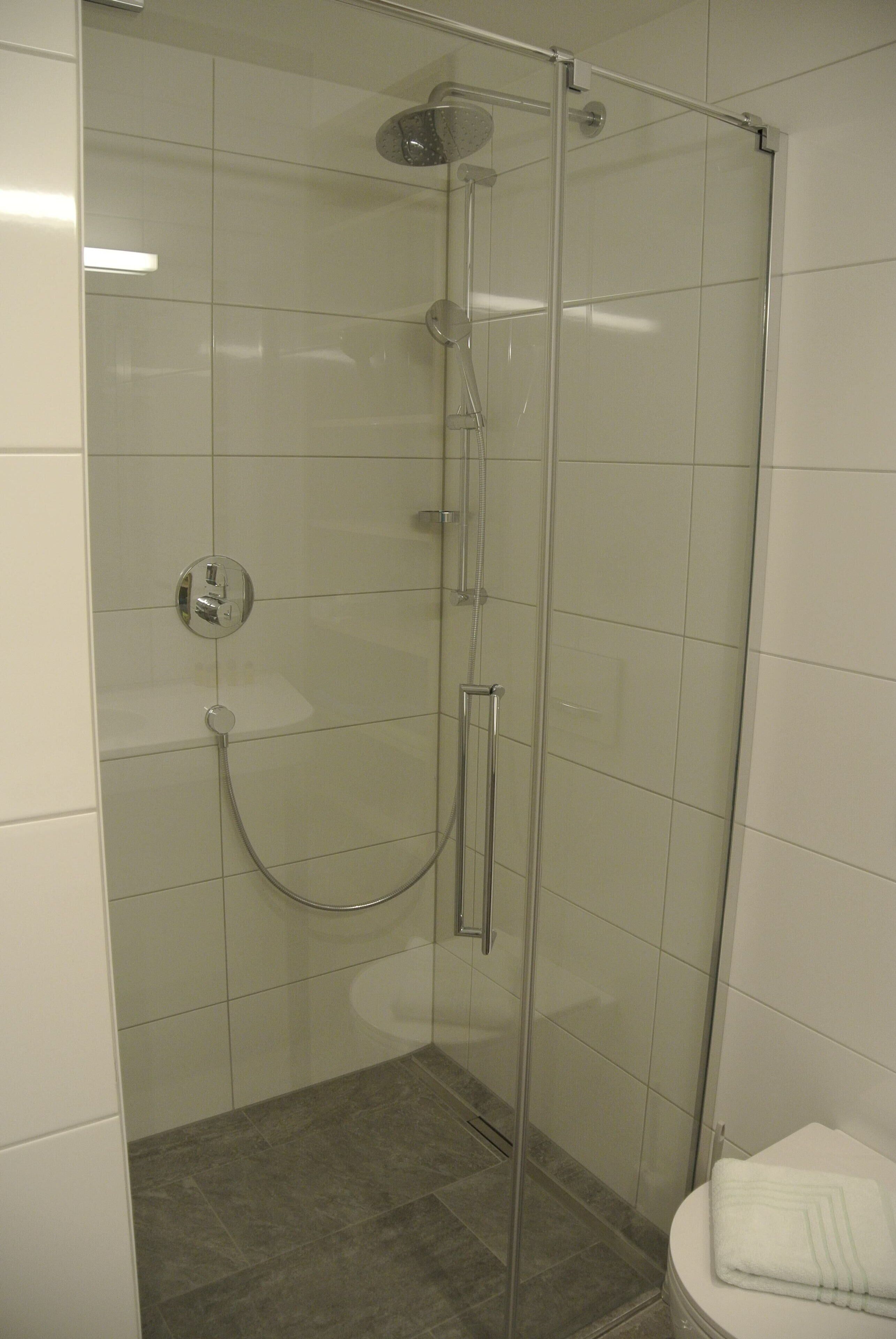 A glass-enclosed shower with a handheld showerhead and a wall-mounted faucet.
