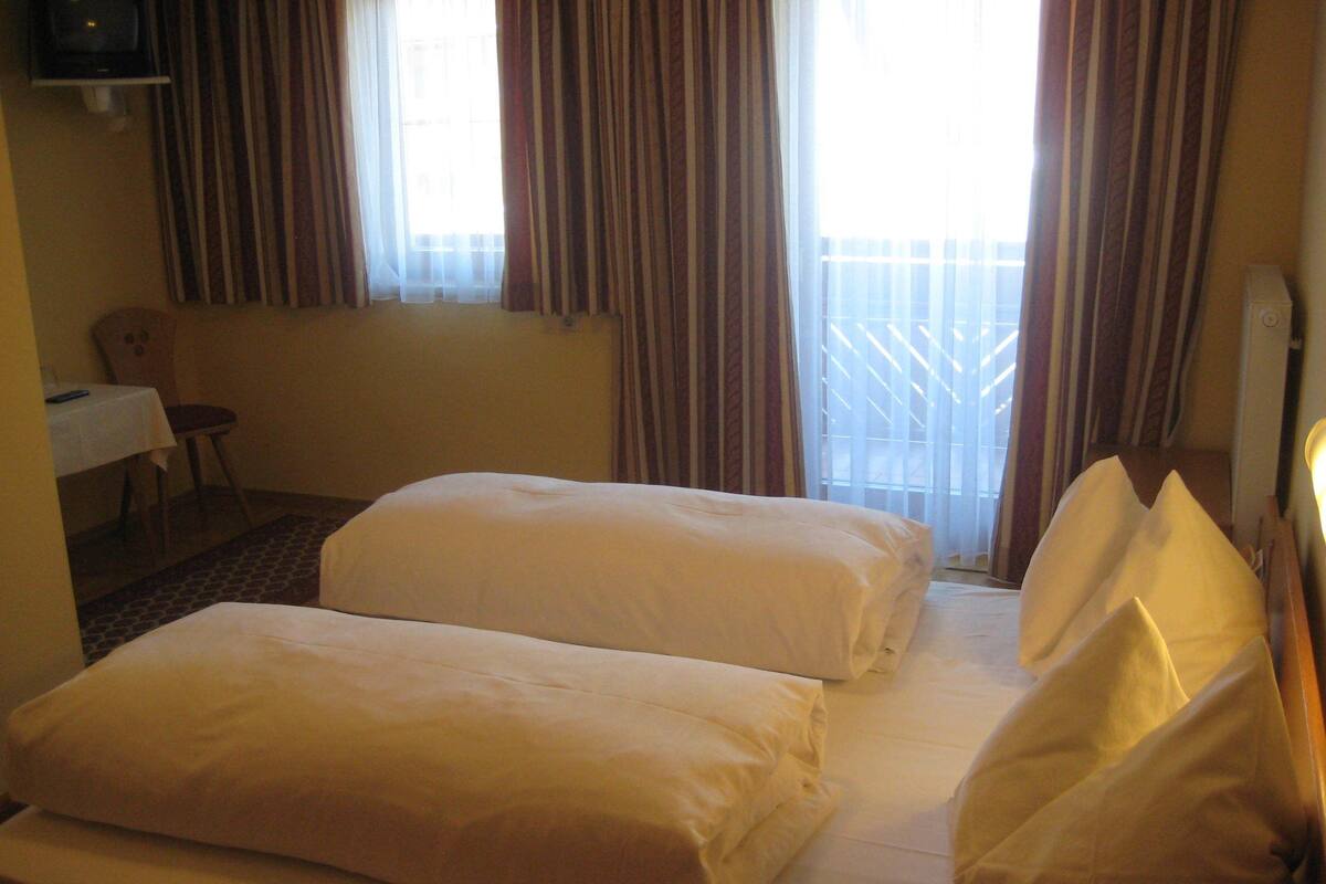 Una habitación de hotel con dos camas, una mesita con una silla y un televisor fijado en la pared.