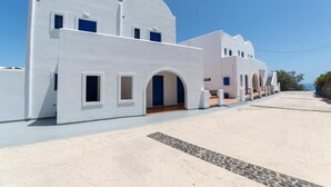 A white building with multiple arched doorways and windows, a flat roof, and a clear sky. - Sigal Villa (Santorini)