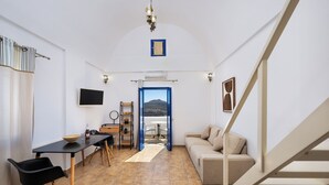 A compact living space with a dining area, a sofa, a staircase, and a view through an open door. - Sigal Villa (Santorini)