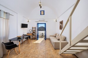 A compact living space with a dining area, a sofa, a staircase, and a view through an open door. - Sigal Villa (Santorini)