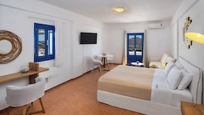 A hotel room with a bed, a desk, a chair, a TV, and a view of the outside. - Sigal Villa (Santorini)