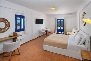 A hotel room with a bed, a desk, a chair, a TV, and a view of the outside. - Sigal Villa (Santorini)