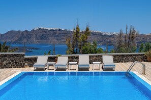 Una piscina con sillas de descanso, un muro de piedra y vistas a montañas y agua.